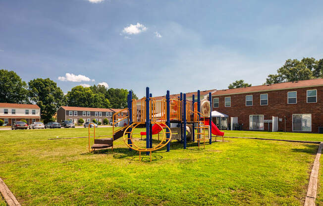 A playground with a swing set and a red slide in the foreground and apartment buildings in the background.