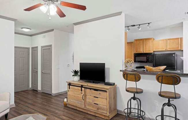 A living room with a television on a wooden stand and a bar area with stools.