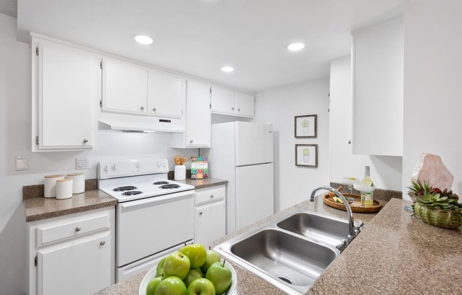 a kitchen with white appliances and white cabinets and a sink with apples on the counter