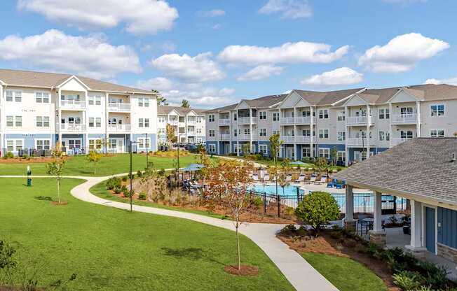 A large grassy area in front of apartment buildings with a pool and trees.