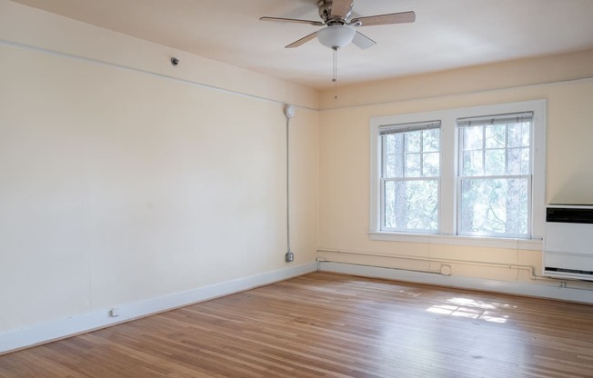 an empty room with a ceiling fan and two windows