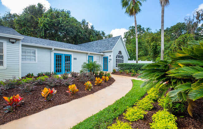 A small house with a blue door is surrounded by a garden with yellow flowers.