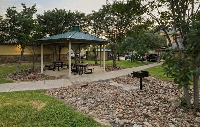 a gazebo in a park with benches and a grill