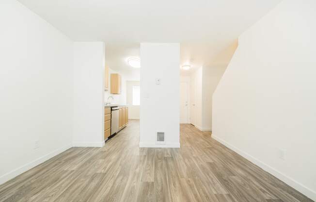 a living room and kitchen with white walls and wood flooring