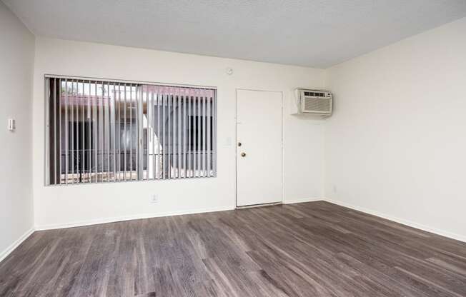 the living room of an apartment with a large window and wood flooring