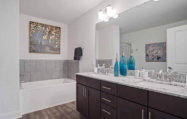 A bathroom with a white tub, brown cabinets, and a painting on the wall.