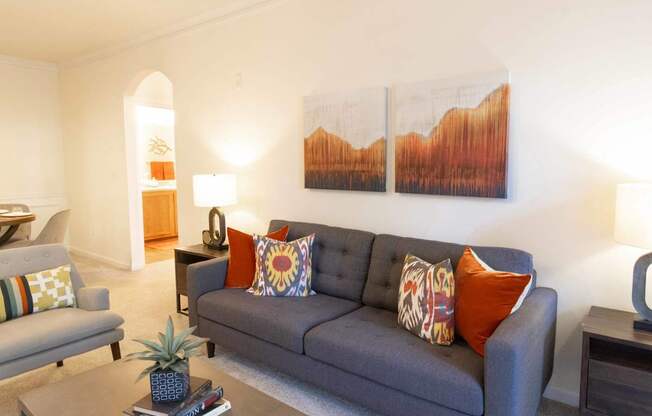 A living room with a grey couch and a painting on the wall.