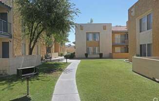 a walkway between two apartment buildings with a lawn and a tree