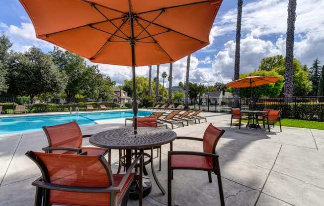 Community swimming pool area with table, chairs and sun umbrellas 