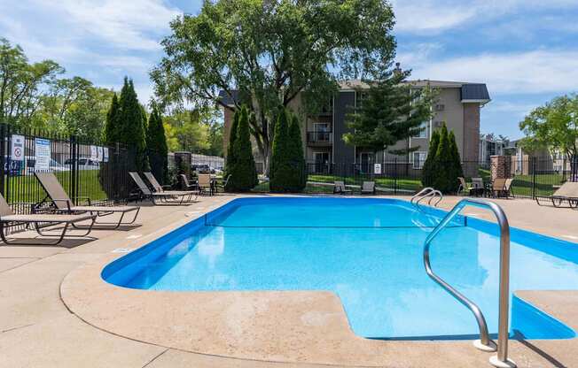 A blue swimming pool surrounded by trees and chairs.