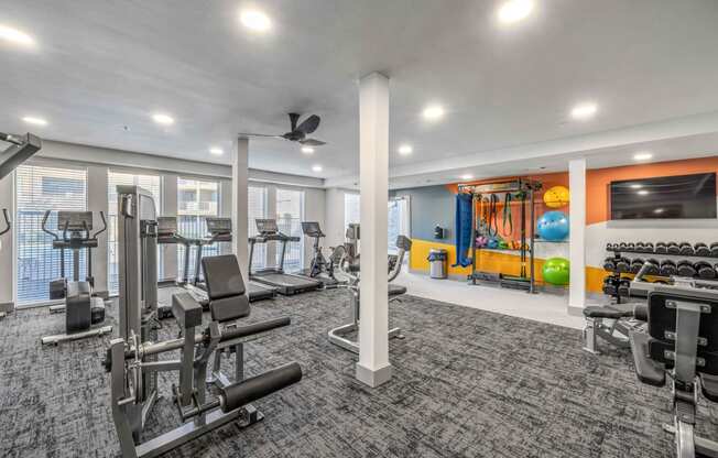 a gym with exercise equipment and a tv in a building with windows