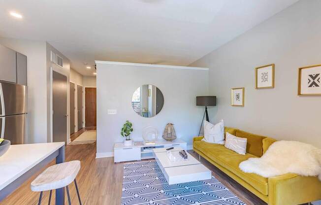 A living room with a yellow couch and a round mirror on the wall.