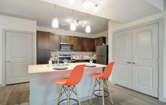 a kitchen with white cabinets and a white island with two orange chairs