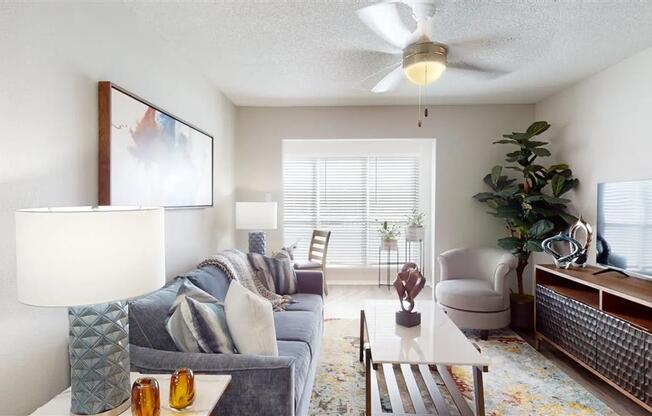 A living room with a grey couch, a white coffee table, a ceiling fan, and a painting on the wall.
