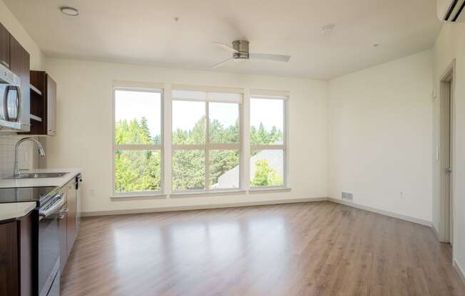 an empty living room with a large window and a kitchen