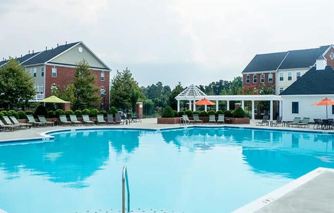 a large blue pool with lounge chairs and umbrellas in front of a building at Flats at West Broad Village, Glen Allen Virginia