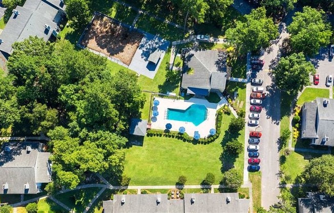 A bird's eye view of a residential area with houses, a swimming pool, and parked cars.