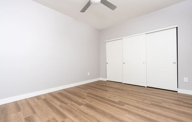 a living room with white walls and wood flooring and a ceiling fan