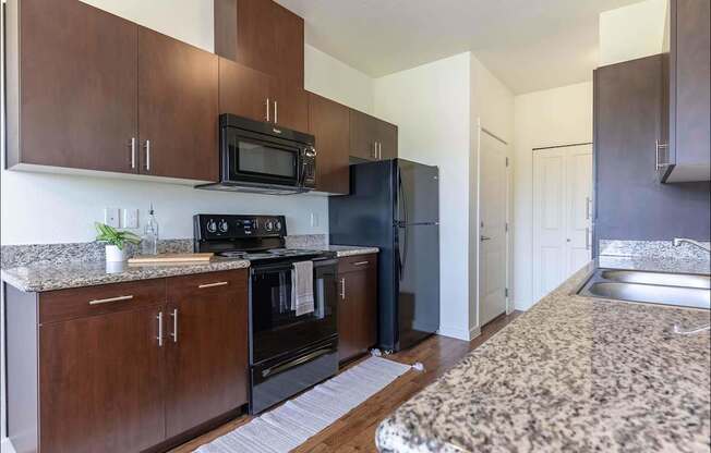 A kitchen with dark wood cabinets and black appliances at Riverplace Apartment Homes, Independence