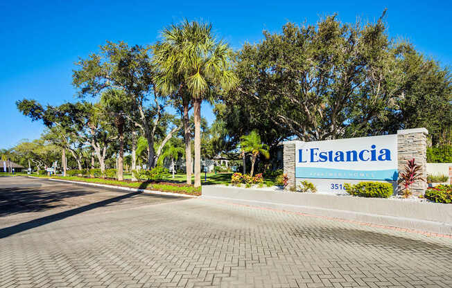 A sign that says L'Estancia in front of some trees.