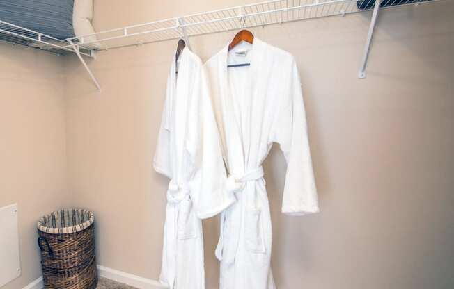 two white robes hanging on a rack in a closet