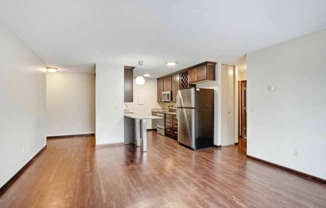 an empty living room and kitchen with wood flooring and a stainless steel refrigerator