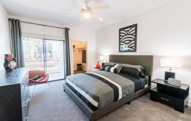 A bedroom with a dresser and window and ceiling fan and large bed