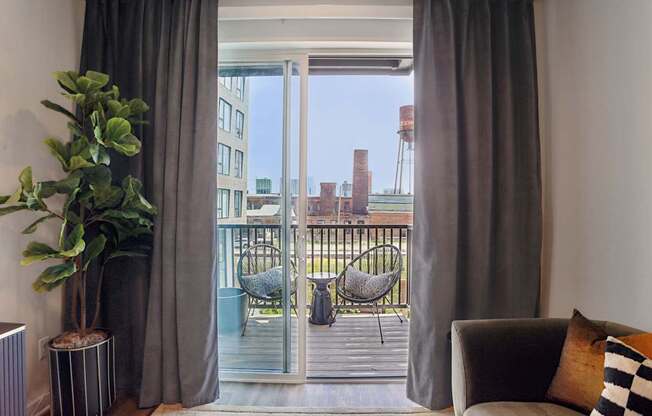 A living room with a grey couch and a view of a balcony with chairs.