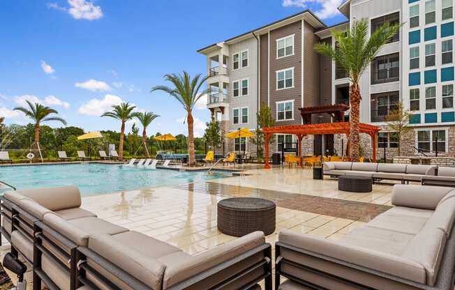 a swimming pool with lounge chairs and umbrellas in front of an apartment building