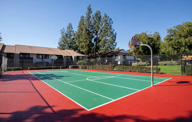 A red and green tennis court with a basketball hoop in the background.