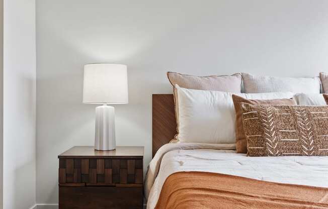 A bed with a white comforter and a lamp on a side table.
