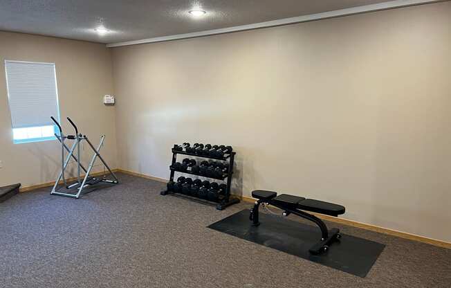 a small exercise room with weights and a bench at Bluemont Village Apartments, Fargo, 58104
