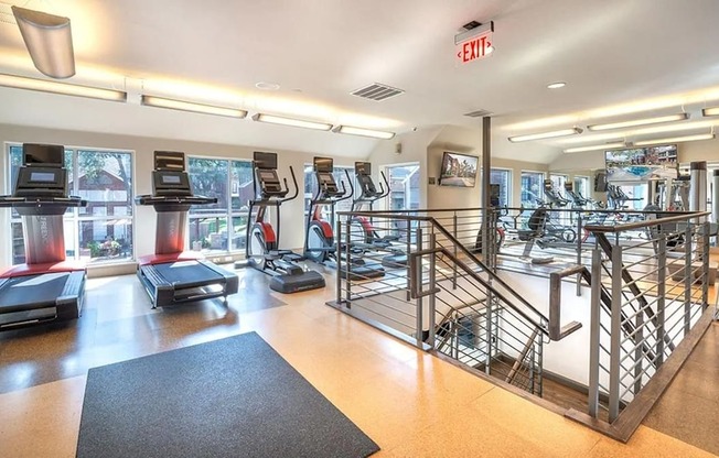 A fitness center here at Lakewood on the Trail with bright lighting, multiple treadmills and ellipticals, mirrored walls, rubber flooring, and large windows overlooking the community.