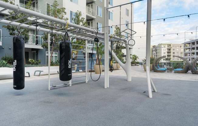 A gym setup with punching bags and rings in front of apartment buildings.