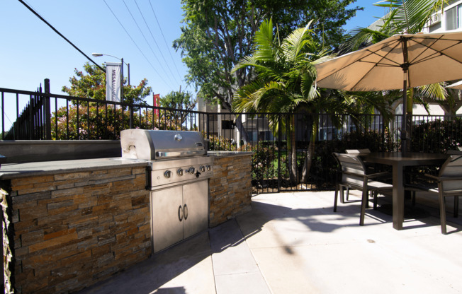 A patio with a grill and chairs under an umbrella.