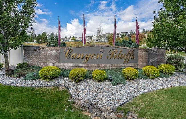 Apartments Spokane WA - Canyon Bluffs - Monument Sign Surrounded by Lush Landscaping and Flags