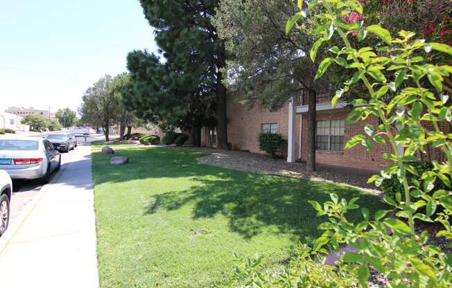 a grassy area with trees and bushes in front of a brick building