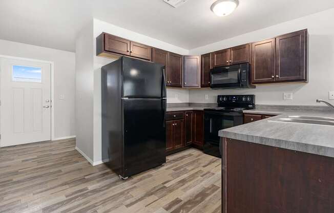 A black refrigerator stands in a kitchen with wooden cabinets and a marble countertop.