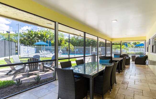 A patio with a glass table surrounded by chairs and a pool in the background.