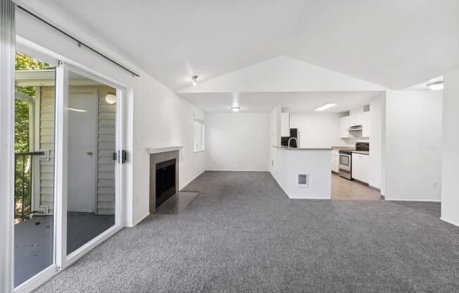 an empty living room with a fireplace and a kitchen