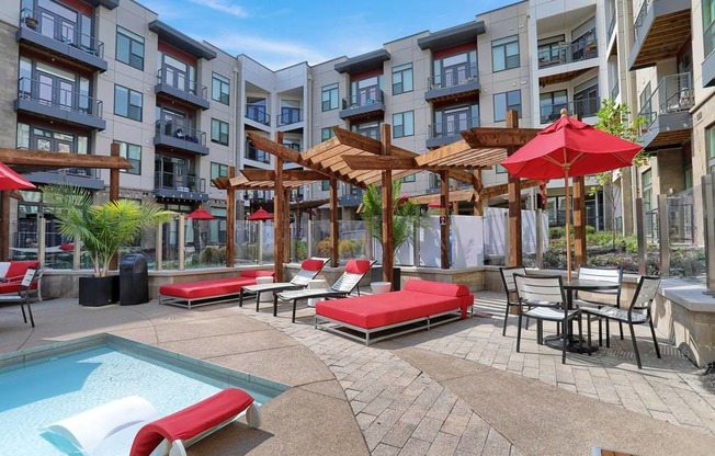 a pool with lounge chairs and umbrellas in front of an apartment building