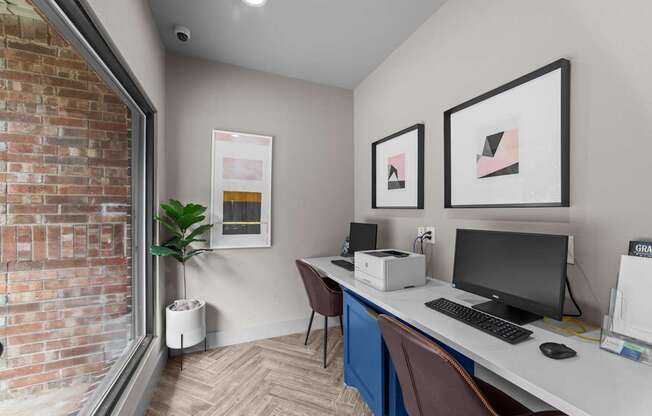 A room with a desk, a computer, and two framed pictures on the wall.