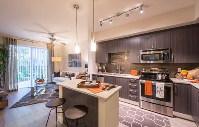 Model kitchen at our apartments in Miami, featuring stainless steel appliances, grey cupboards, and a view of the living room.
