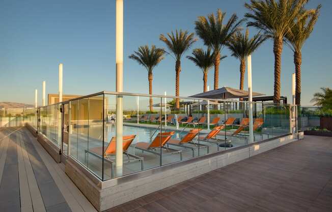 a pool with orange lounge chairs and palm trees in the background