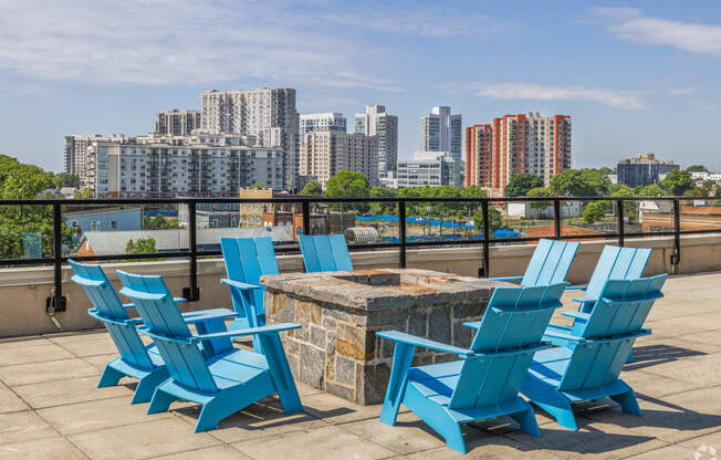 a deck with blue chairs and a fire pit with a view of the city