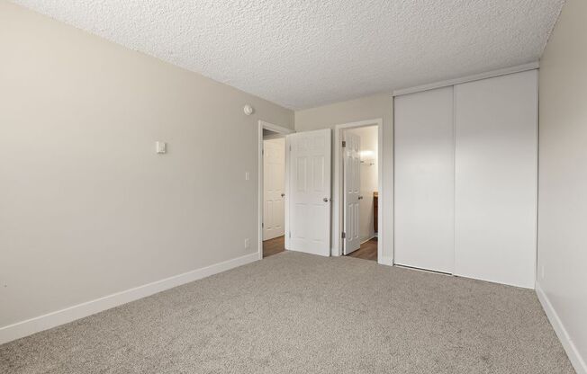 a bedroom with white walls and carpet and a door to a closet