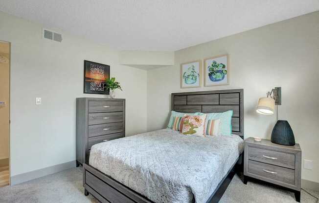 A bedroom with a bed, nightstand, and two pictures on the wall.