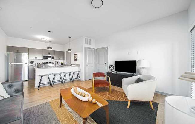 A modern living room with a white sofa, a wooden coffee table, and a kitchen area in the background.