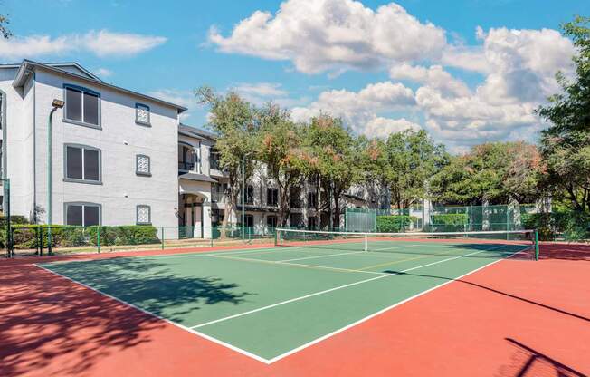 A tennis court is located in front of a white building.