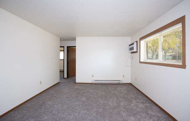 an empty living room with a large window and white walls. Fargo, ND Pacific South Apartments